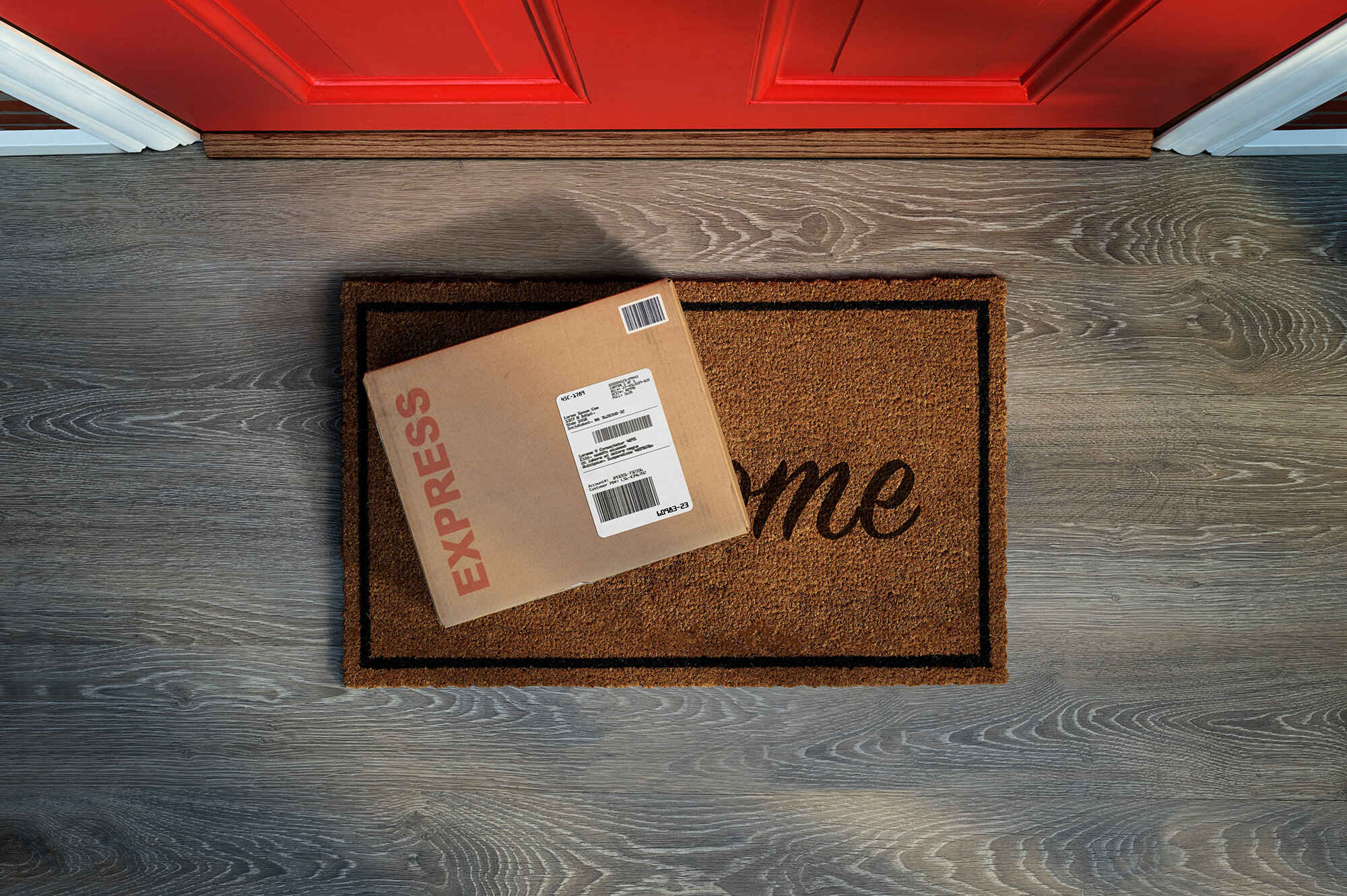 Ein Paket liegt auf einem Fußmatte mit der Aufschrift "Welcome" vor einer roten Haustür.