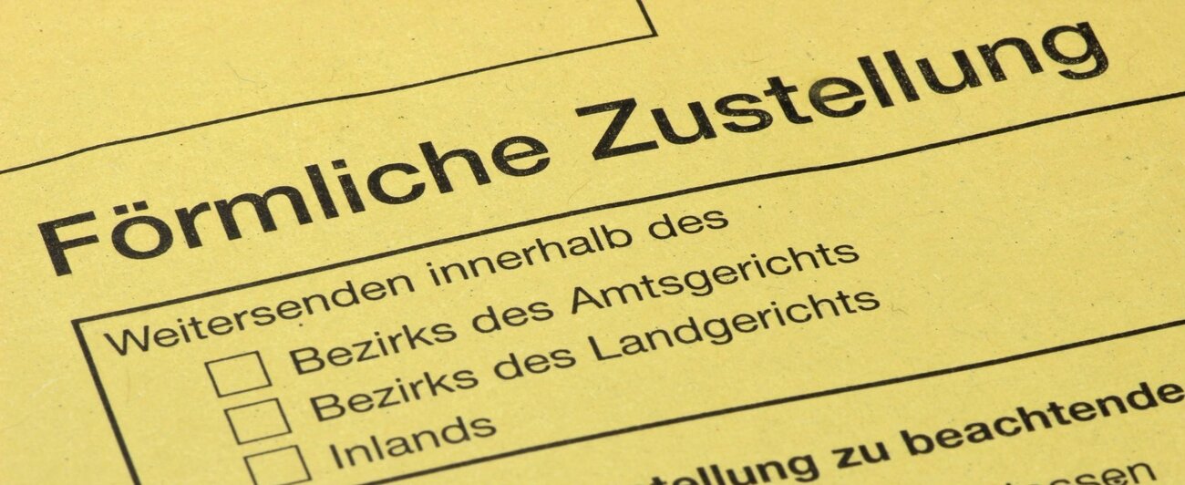 Ein gelber Briefumschlag, der eine förmliche Zustellung signalisiert, liegt auf einem Schreibtisch.